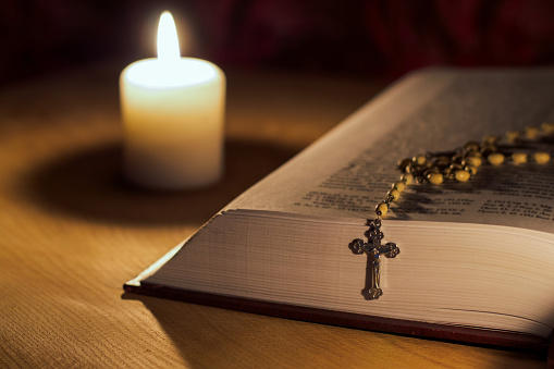 A candle, a bible and a cross a rosary on a wooden table